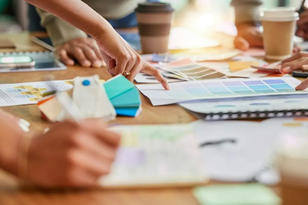 Color, creative meeting and hands of business people on desk for branding design, strategy and mark